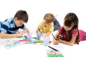 Three children brothers and their sister laying on the floor quietly entertaining themselves by drawing and coloring their favorite picture.